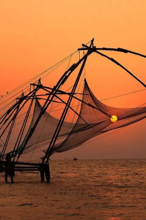 Chinese fishing nets at sunset in Fort Kochi, Kerala, with an orange sky over the Arabian Sea.